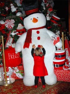 Frosty_HotelDel This is a photo of a toddler reaching up to pull on Frosty the Snowman's big red pom-pom buttons. Frosty is a six foot tall stuffed toy.